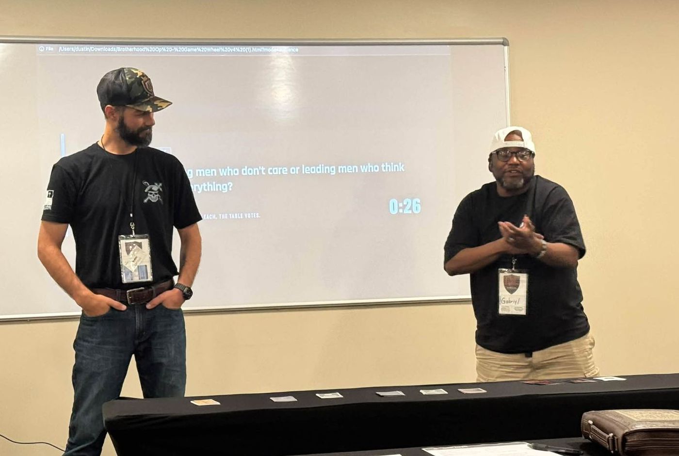 Two men running a round of The Brotherhood Op in front of a room